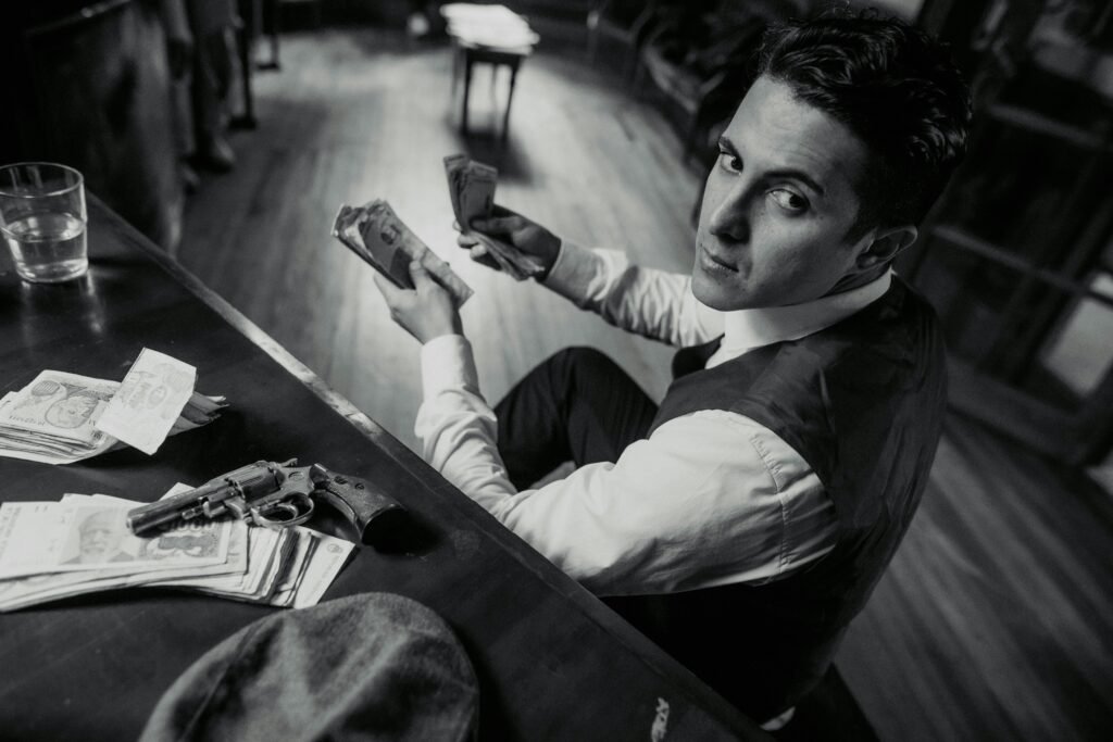 A man counting money with a gun on the desk in a vintage, mafia-themed setting.